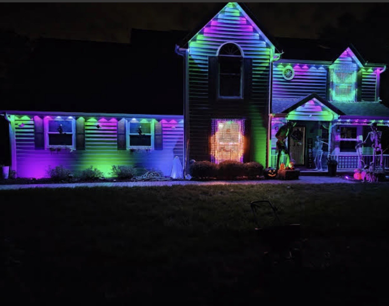 House with purple, green, and blue soffit puck lights and Halloween decor